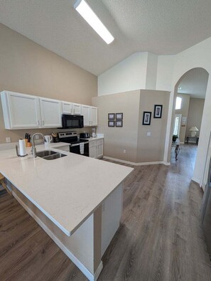 A modern kitchen with white cabinetry, a large island, and a microwave.