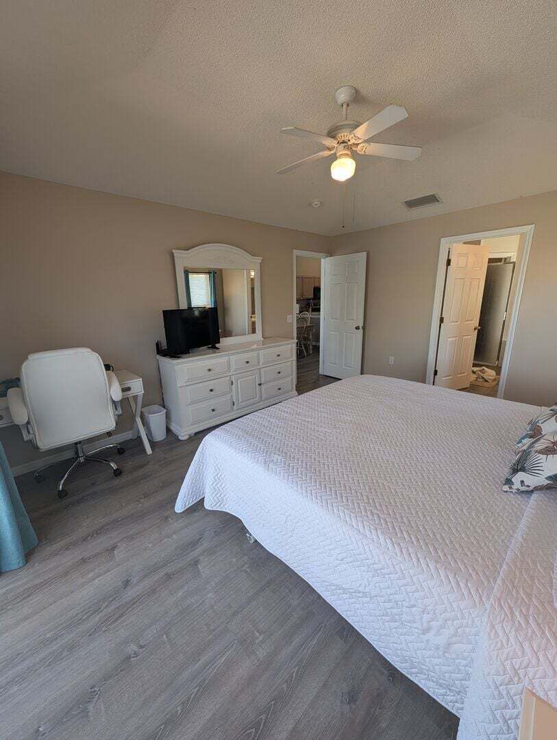 A bedroom with a bed, a desk, a chair, a television, and a ceiling fan.