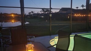 A covered outdoor seating area with a pool, a lantern, and a view of a residential area with houses and a clear sky. - Brand new private pool with lake view minutes to the parks! (Kissimmee)