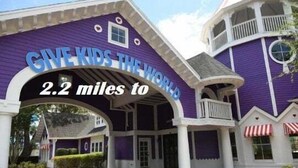 A large, purple building with a sign reading "GIVE KIDS THE WORLD" and "2.2 miles to". - Brand new private pool with lake view minutes to the parks! (Kissimmee)
