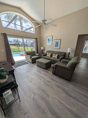 A spacious living room with a ceiling fan, a large window, and a view of a swimming pool. - Brand new private pool with lake view minutes to the parks! (Kissimmee)