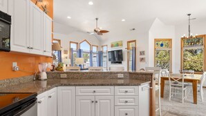Una cocina con armarios blancos, encimeras de granito y una zona de comedor con mesa y sillas de madera.