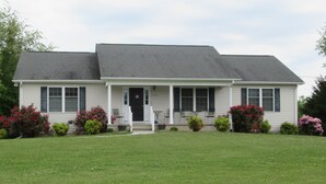 A two-story house with a front porch, a garage, and a well-maintained lawn. - Gorgeous Mtn Views, Perfect for Fall, Near Peaks of Otter, D-Day Memorial (Bedford)
