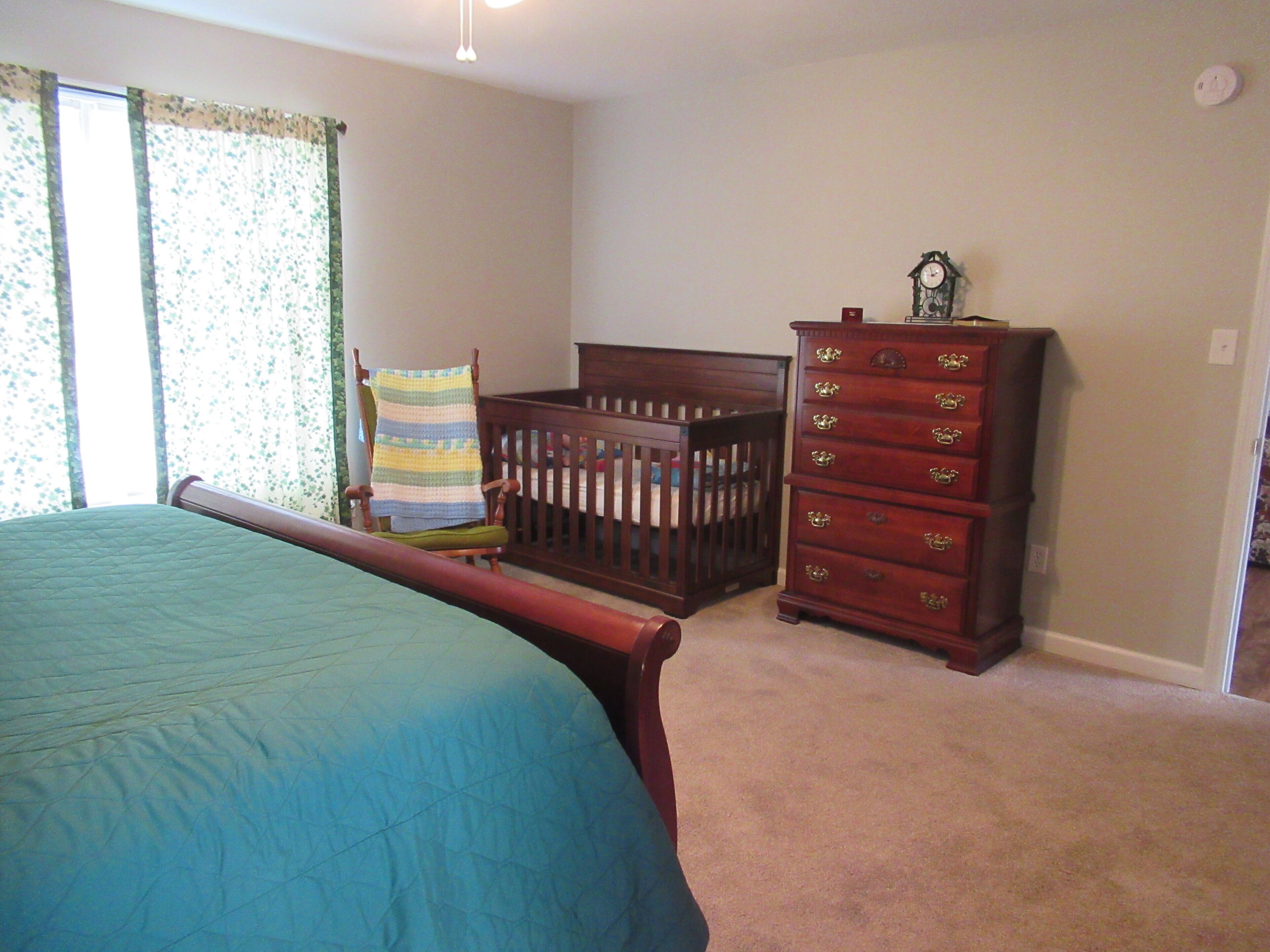A bedroom with a bed, a crib, a dresser, and a chair.