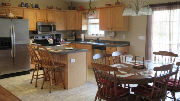 A kitchen with wooden cabinets, a refrigerator, microwave, and a dining area with a table and chairs. - Gorgeous Mtn Views, Perfect for Fall, Near Peaks of Otter, D-Day Memorial (Bedford)