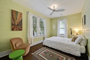 A bedroom with a bed, a chair, a small table, and a ceiling fan.