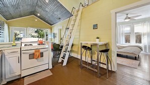 Cocina compacta con estufa, horno y una escalera que lleva a una zona de dormir en un altillo.