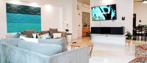 Una sala de estar moderna con un sofá gris, una mesa de centro de madera y un televisor de pantalla plana grande montado en la pared.
