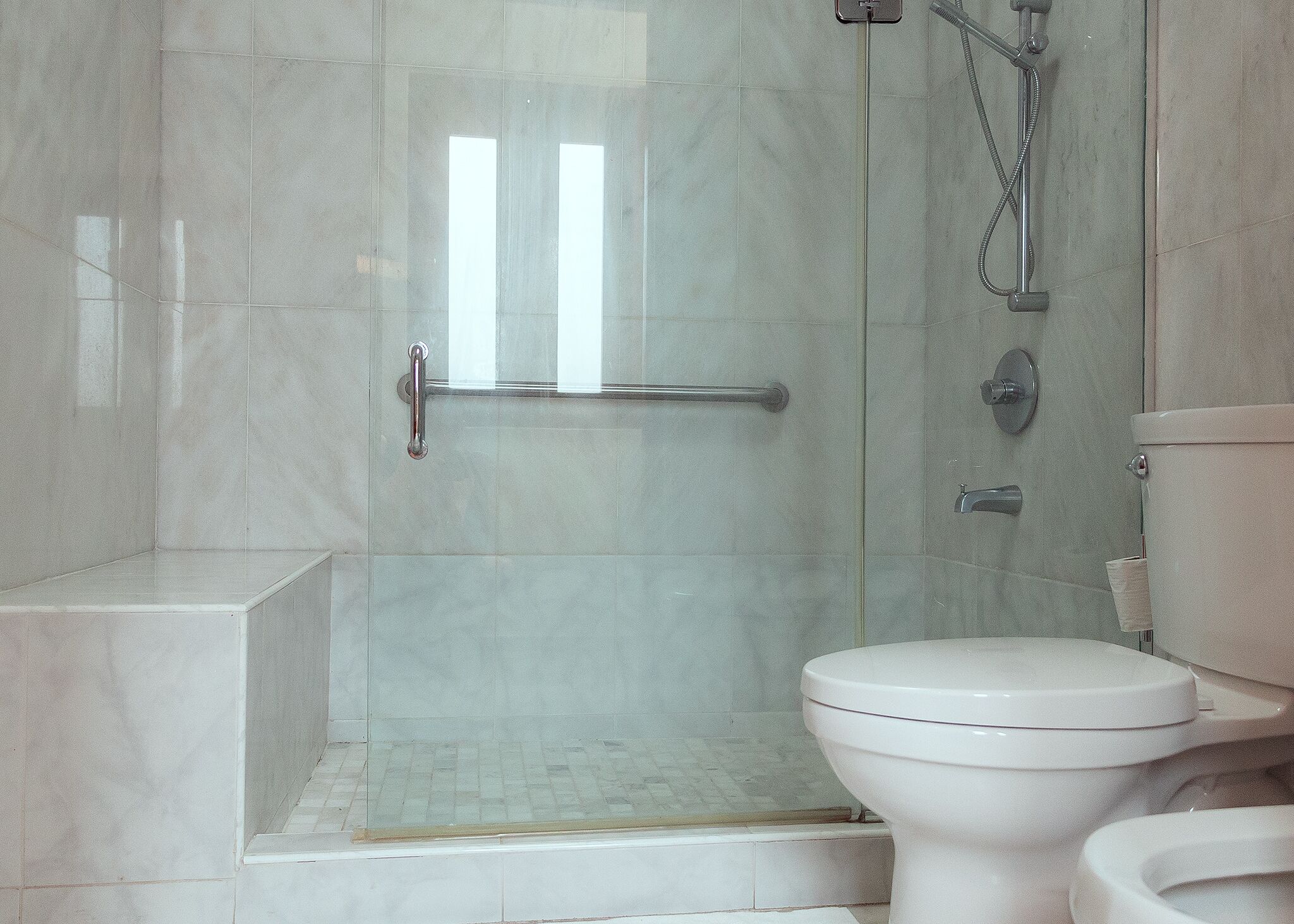 Un bagno con doccia vetrata, un water bianco e pavimento piastrellato.