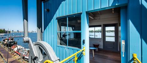 A blue building with a large window and a door, overlooking a body of water with boats.