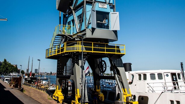 A large crane with a blue and yellow color scheme, situated near a waterfront with boats and a clear blue sky. - Numa Amsterdam The Crane (Amsterdam)