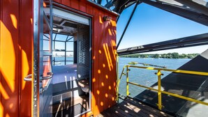 A deck with a glass door leading to a room, a yellow railing, and a view of a river and distant buildings. - Numa Amsterdam The Crane (Amsterdam)