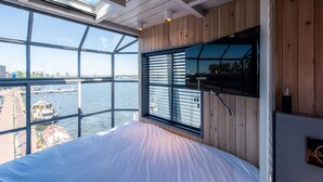 A bedroom with a large window overlooking a body of water and a cityscape. - Numa Amsterdam The Crane (Amsterdam)