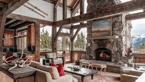 A spacious living room with a stone fireplace, wooden beams, and a view of the mountains. - Ski In/Ski Out | Hot tub | Mountain View (Big Sky)