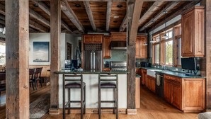A spacious kitchen with wooden cabinets, a central island with bar stools, and large windows providing natural light. - Ski In/Ski Out | Hot tub | Mountain View (Big Sky)