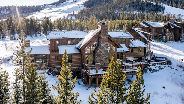 A log cabin-style lodge with a stone chimney, wooden decks, and a view of a snow-covered mountain. - Ski In/Ski Out | Hot tub | Mountain View (Big Sky)