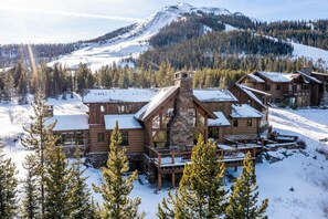 A log cabin-style lodge with a stone chimney, wooden decks, and a view of a snow-covered mountain.