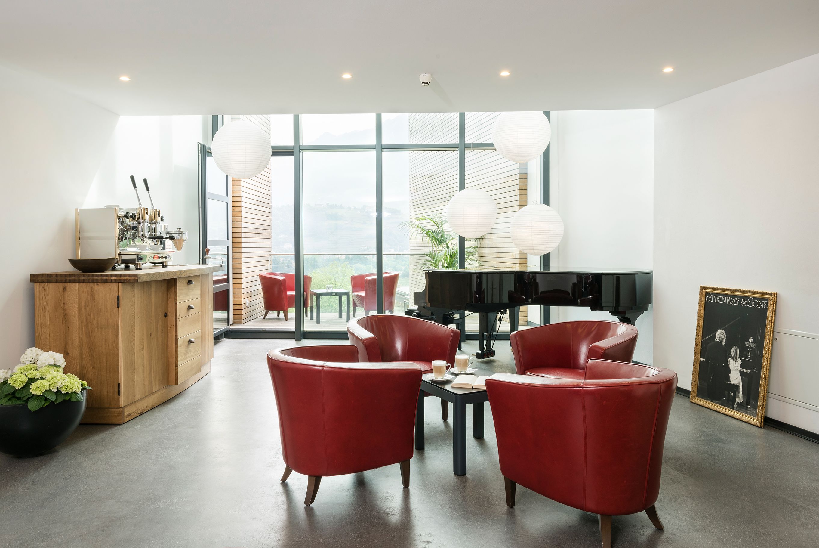 A modern living room with red leather chairs, a piano, and a large window with a view.
