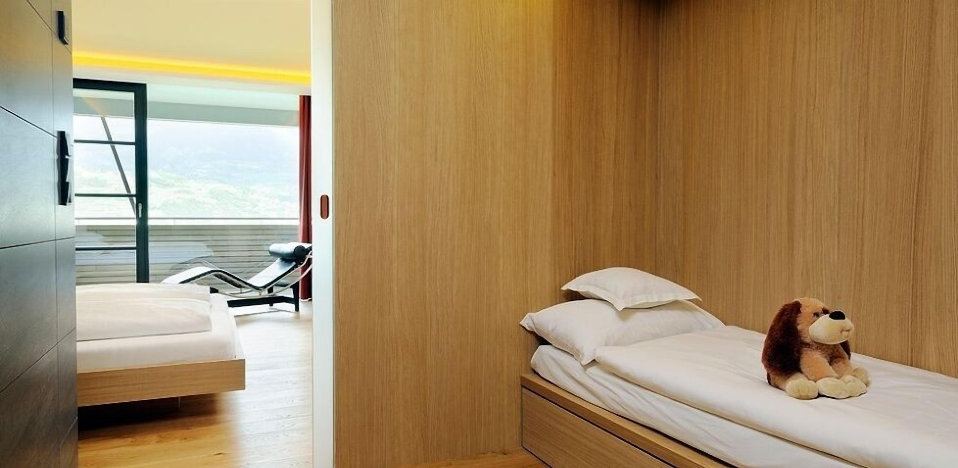 Un dormitorio moderno con un armario de madera, una cama con ropa de cama blanca y un peluche sobre la cama.
