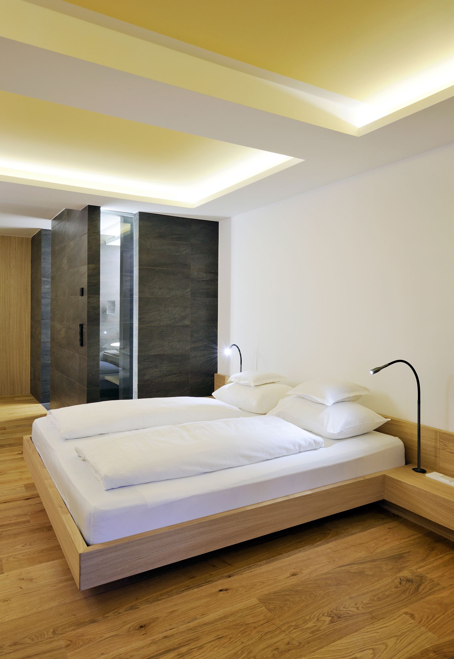 A modern bedroom with a wooden bed, a walk-in closet, and recessed ceiling lighting.