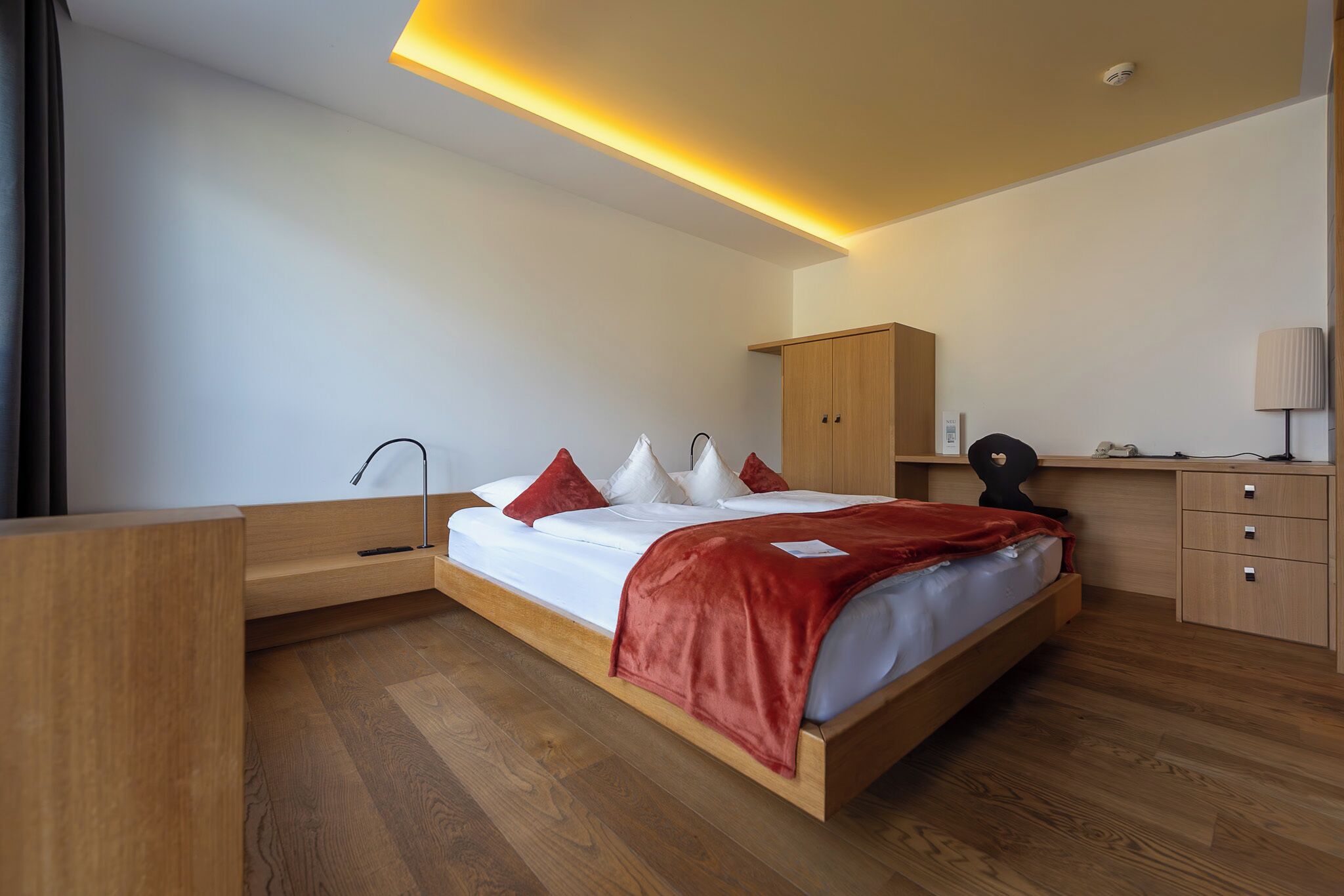 A modern bedroom with a wooden bed, a desk, and a wardrobe.