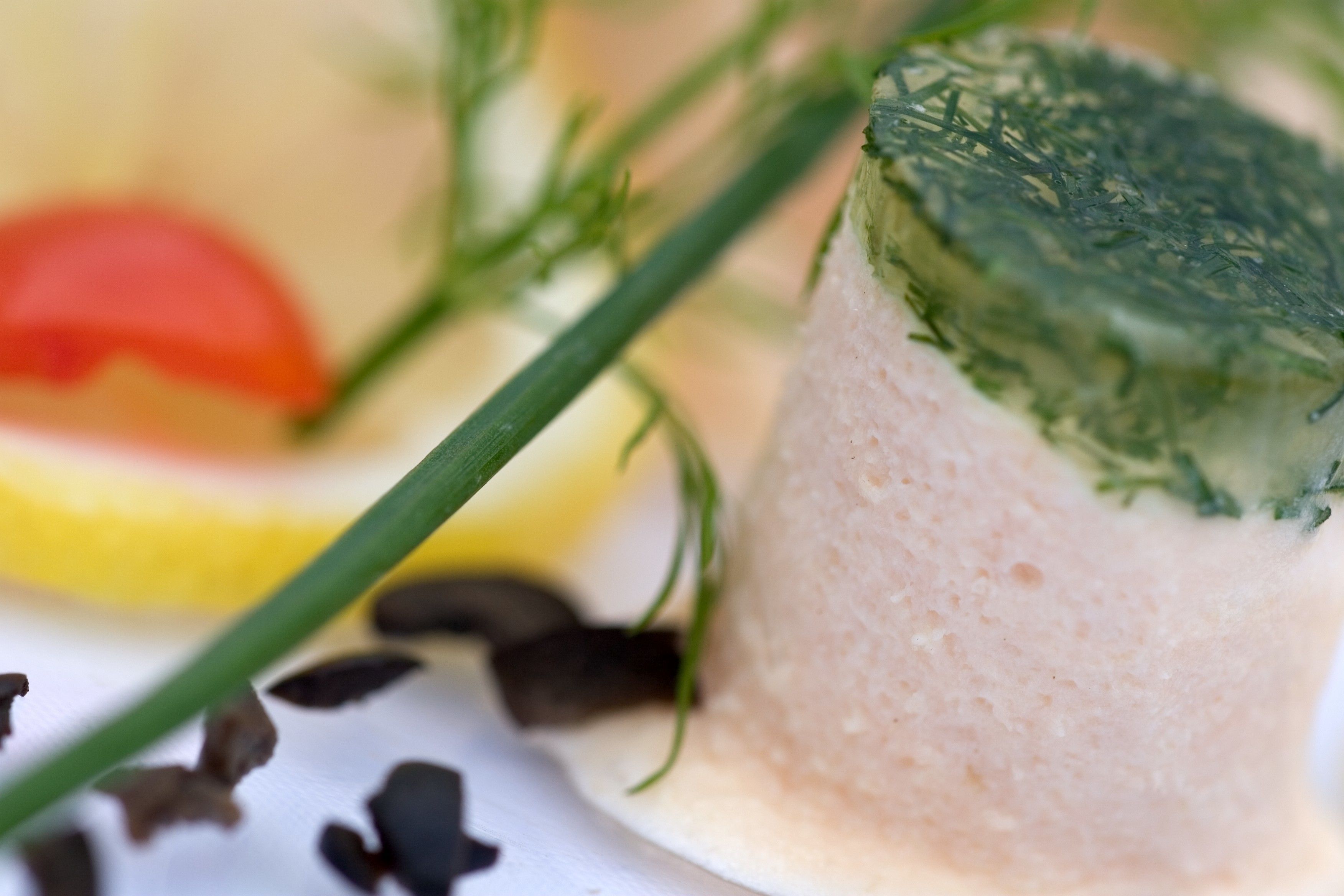 A close-up of a food item with a creamy texture and a green topping, possibly a dessert or appetizer, with a blurred background suggesting a dining setting.