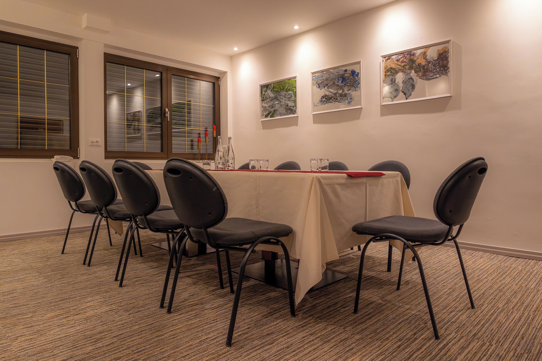 Een vergaderruimte met een lange tafel, zes stoelen en drie kunstwerken in lijsten aan de muur.