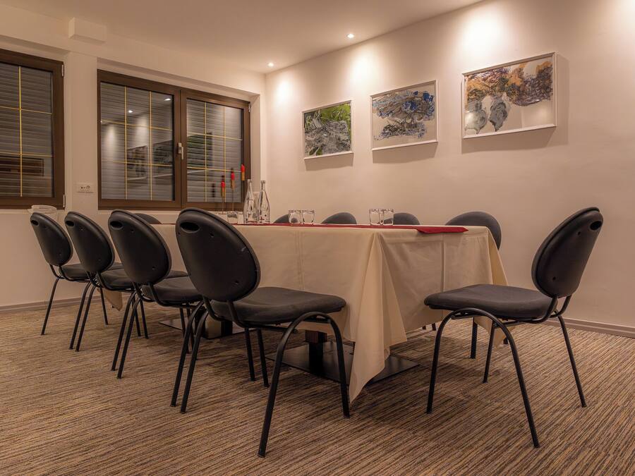Ein Konferenzraum mit einem langen Tisch, sechs Stühlen und drei gerahmten Kunstwerken an der Wand.