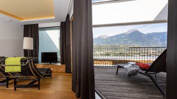 Una habitación de hotel moderna con balcón, sofá, televisor y vistas a las montañas.