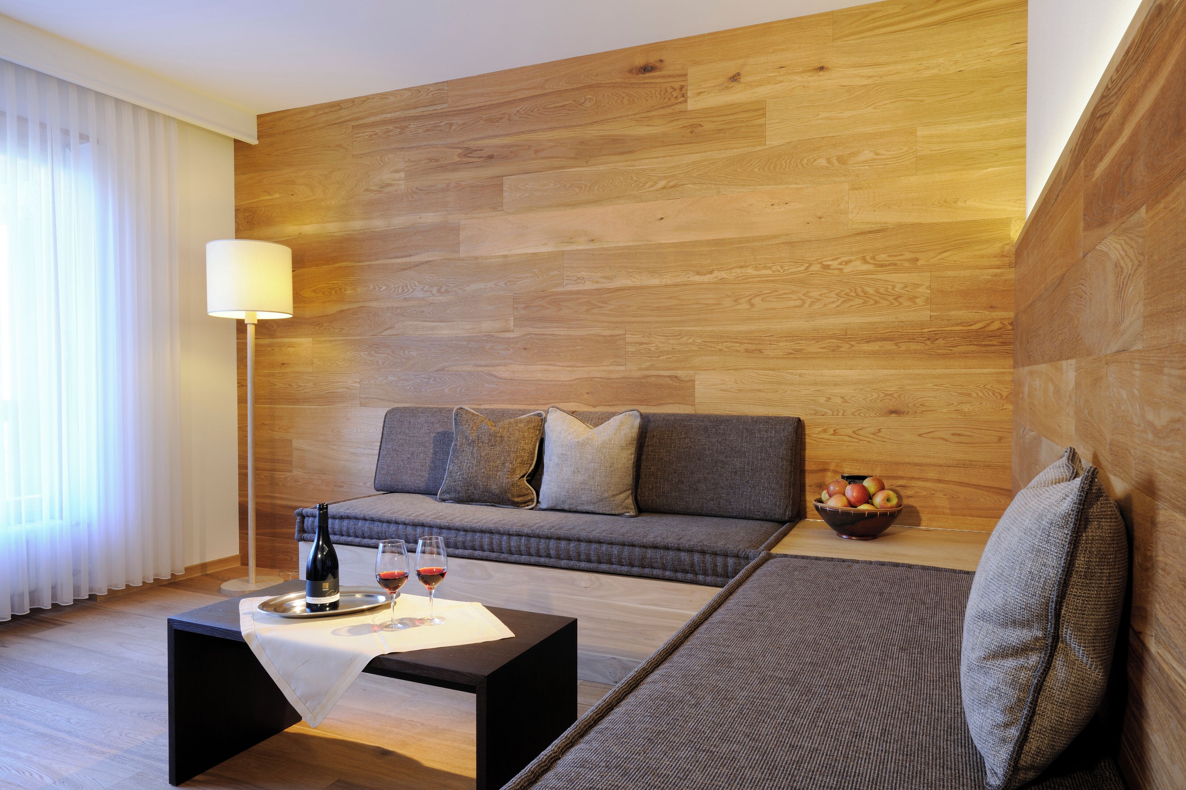 A modern living room with a wooden wall, a grey sofa, a black coffee table, and a lamp.