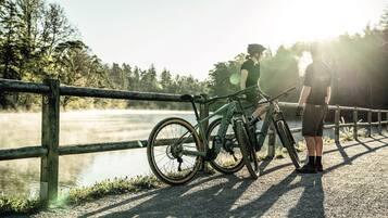 Eine Person steht neben einem Mountainbike auf einer Brücke, im Hintergrund ein See.