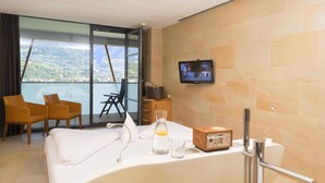 A hotel room with a large bed, a TV mounted on the wall, a chair, a small table, and a view of the mountains through the window.