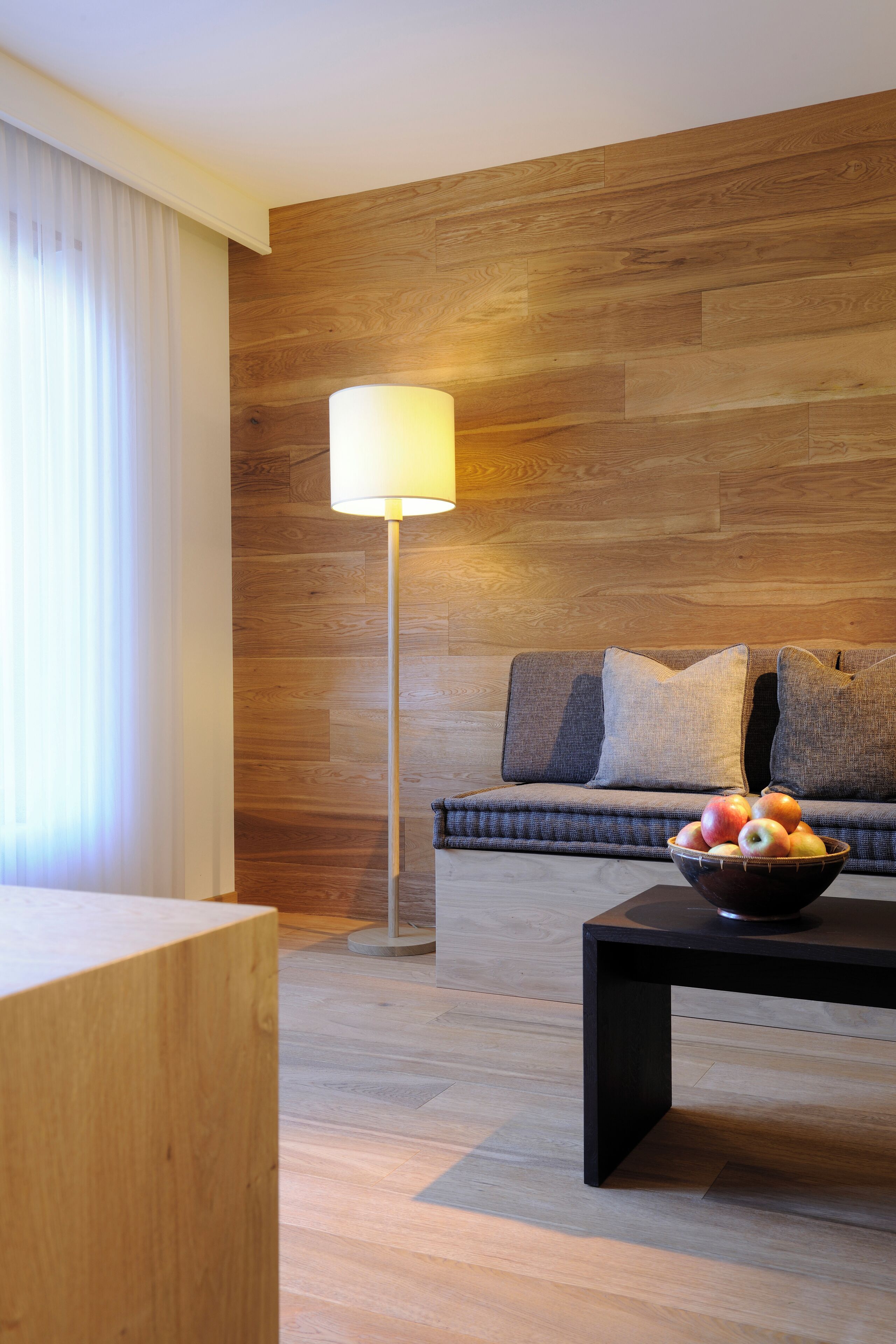 Una sala de estar moderna con piso de madera, un sofá con cojines, una lámpara y un frutero sobre una mesa.