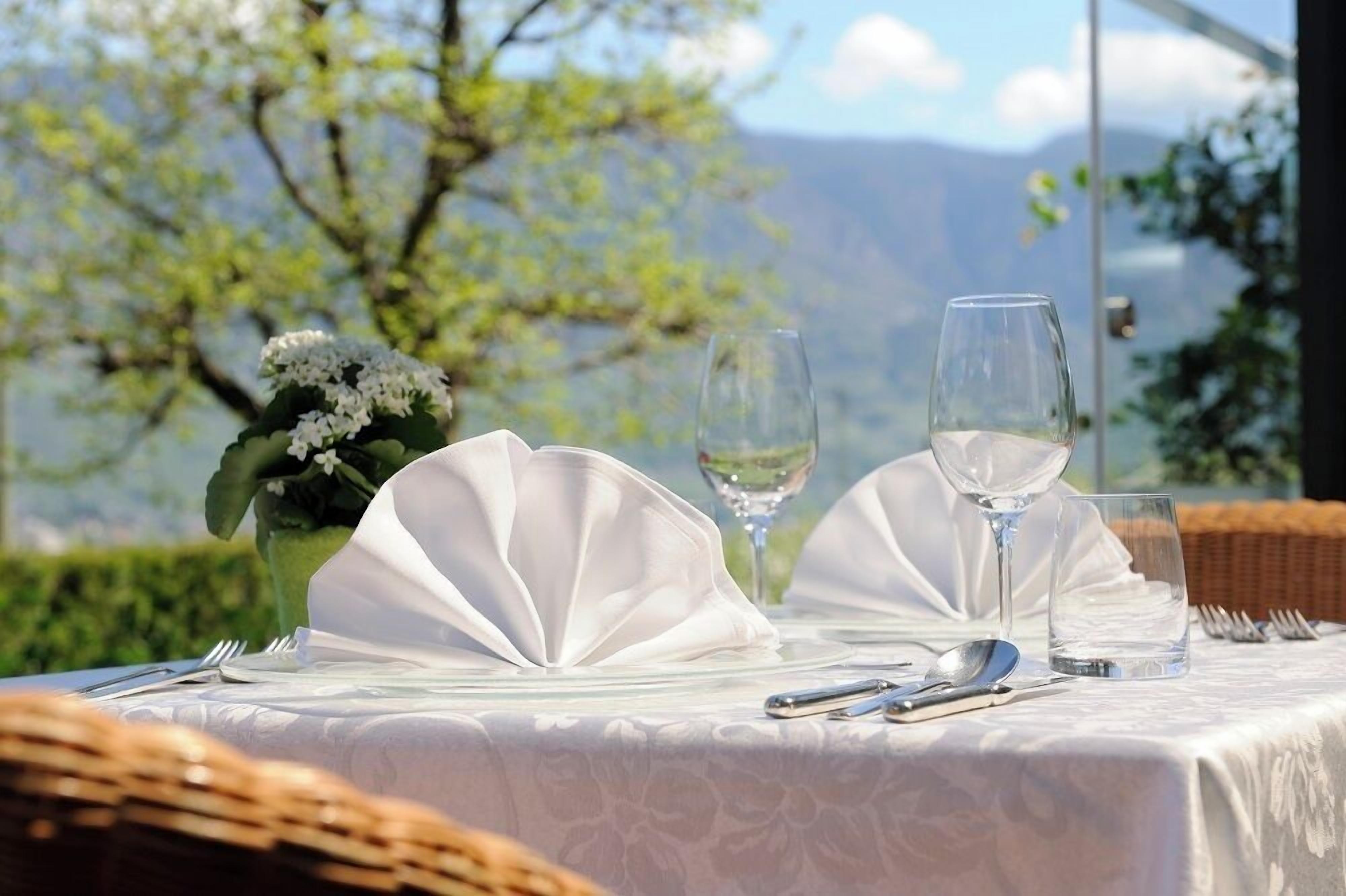 Tavola imbandita con tovaglioli bianchi, bicchieri da vino e posate, con vista su un paesaggio suggestivo.