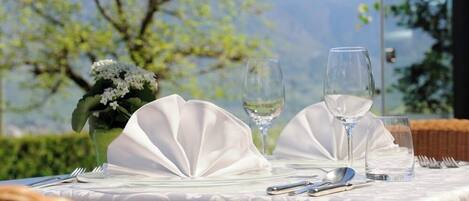 Une table dressée avec des serviettes blanches, des verres à vin et des couverts, offrant une vue sur un paysage magnifique.
