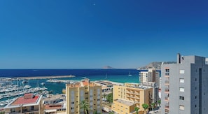 A coastal cityscape with a marina, buildings with balconies, and a clear blue sky.