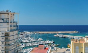 A marina with multiple boats docked, a pier, and a building with balconies.