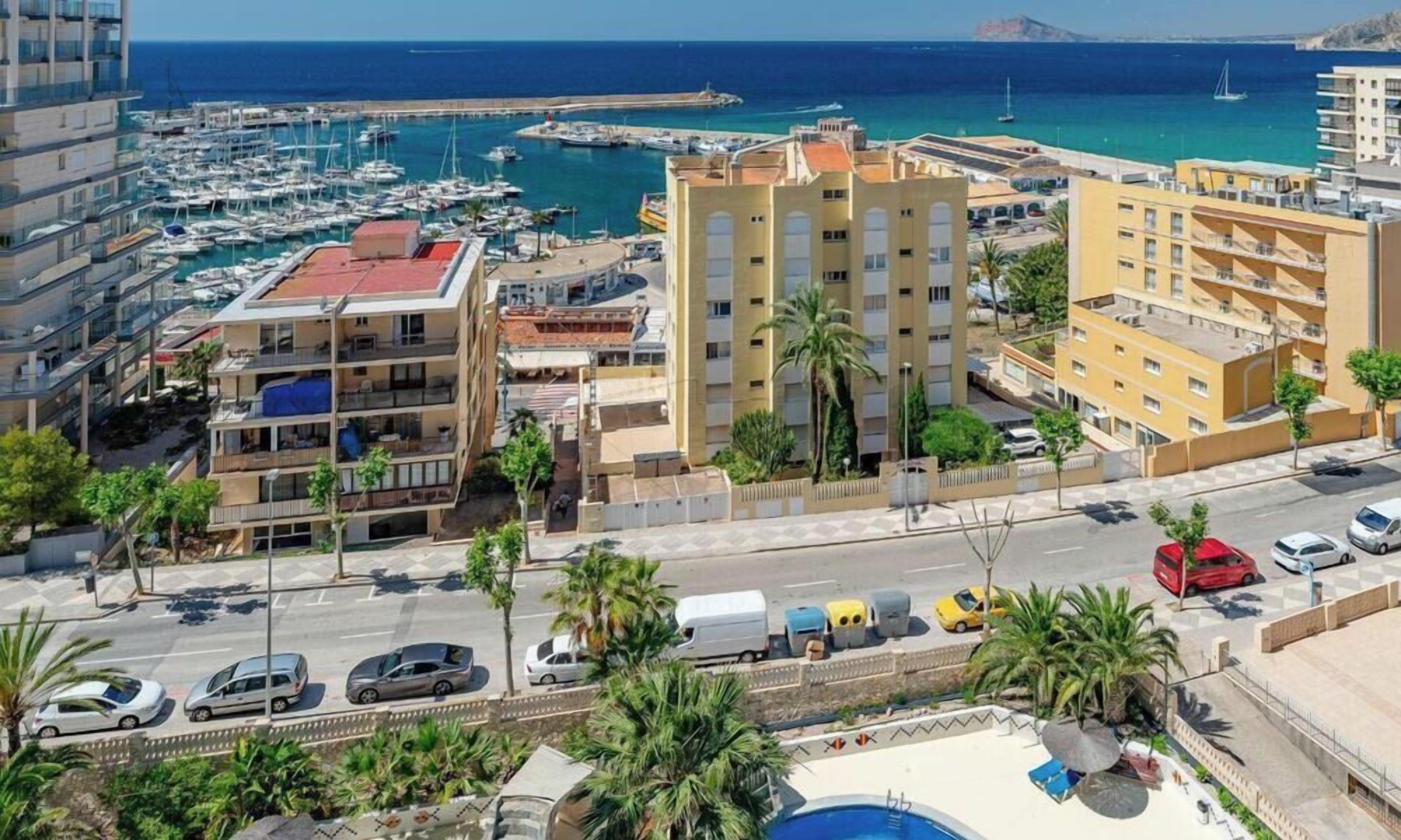 A coastal urban area with a marina, multi-story buildings, and a road with parked cars.