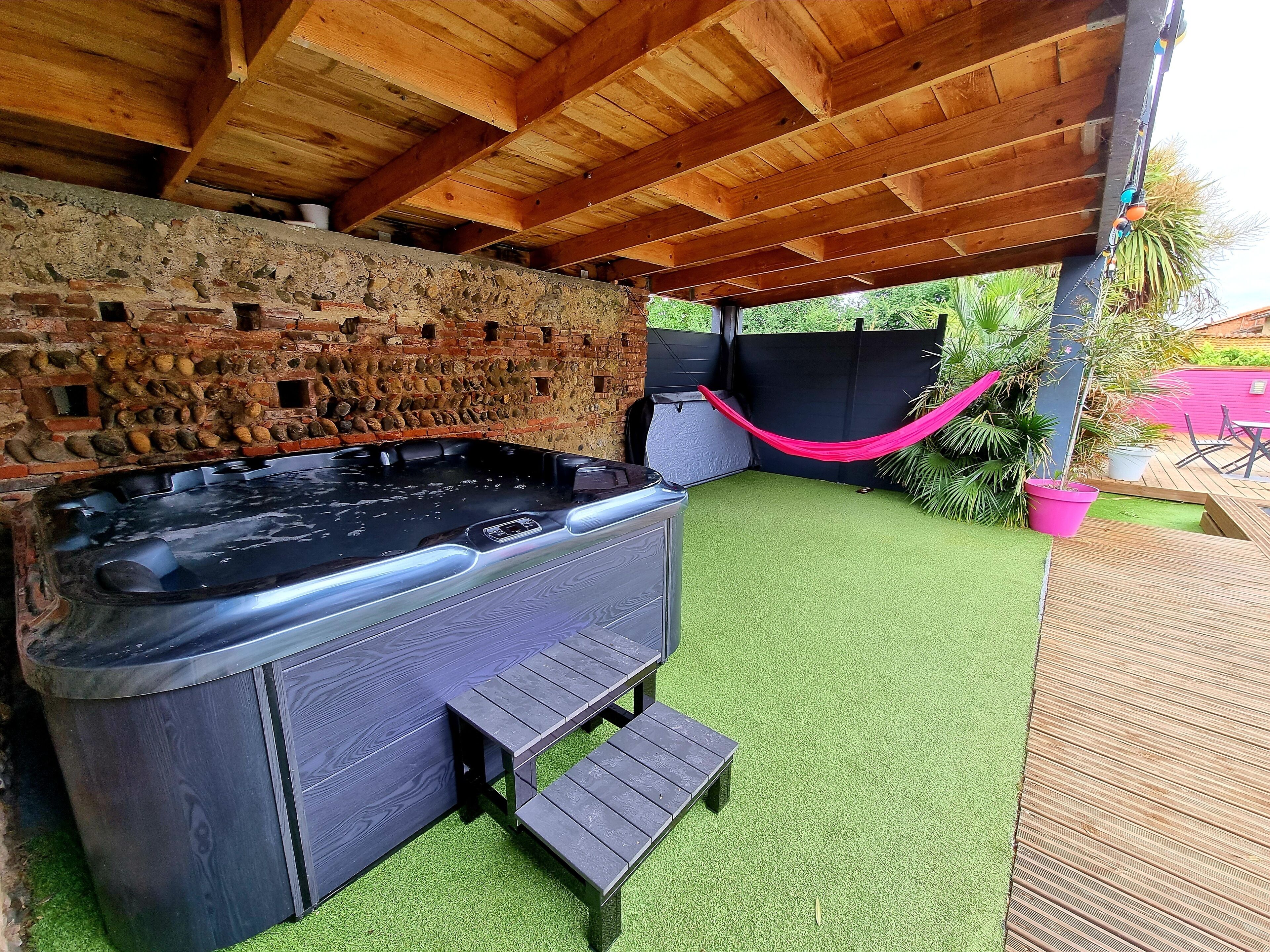 An outdoor hot tub area with a stone wall, wooden ceiling, and artificial grass.