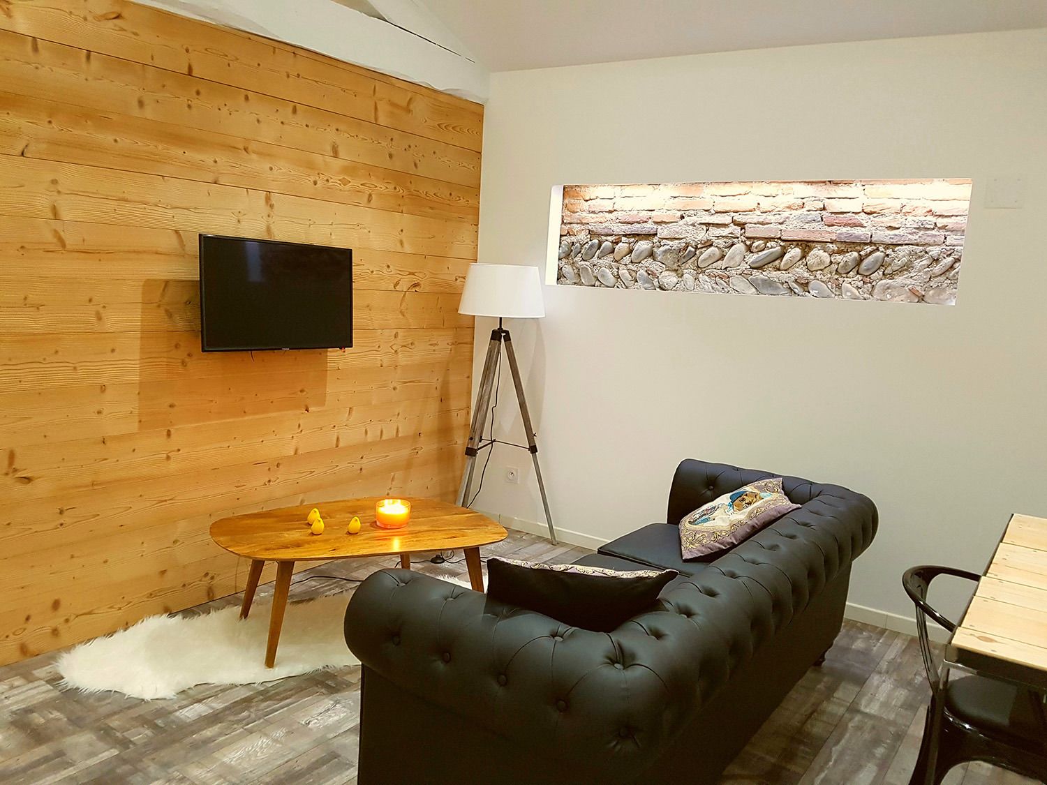 Un salon avec un mur en bois, un canapé en cuir noir, une table basse en bois ornée de bougies, un lampadaire et une œuvre d’art murale en pierre.