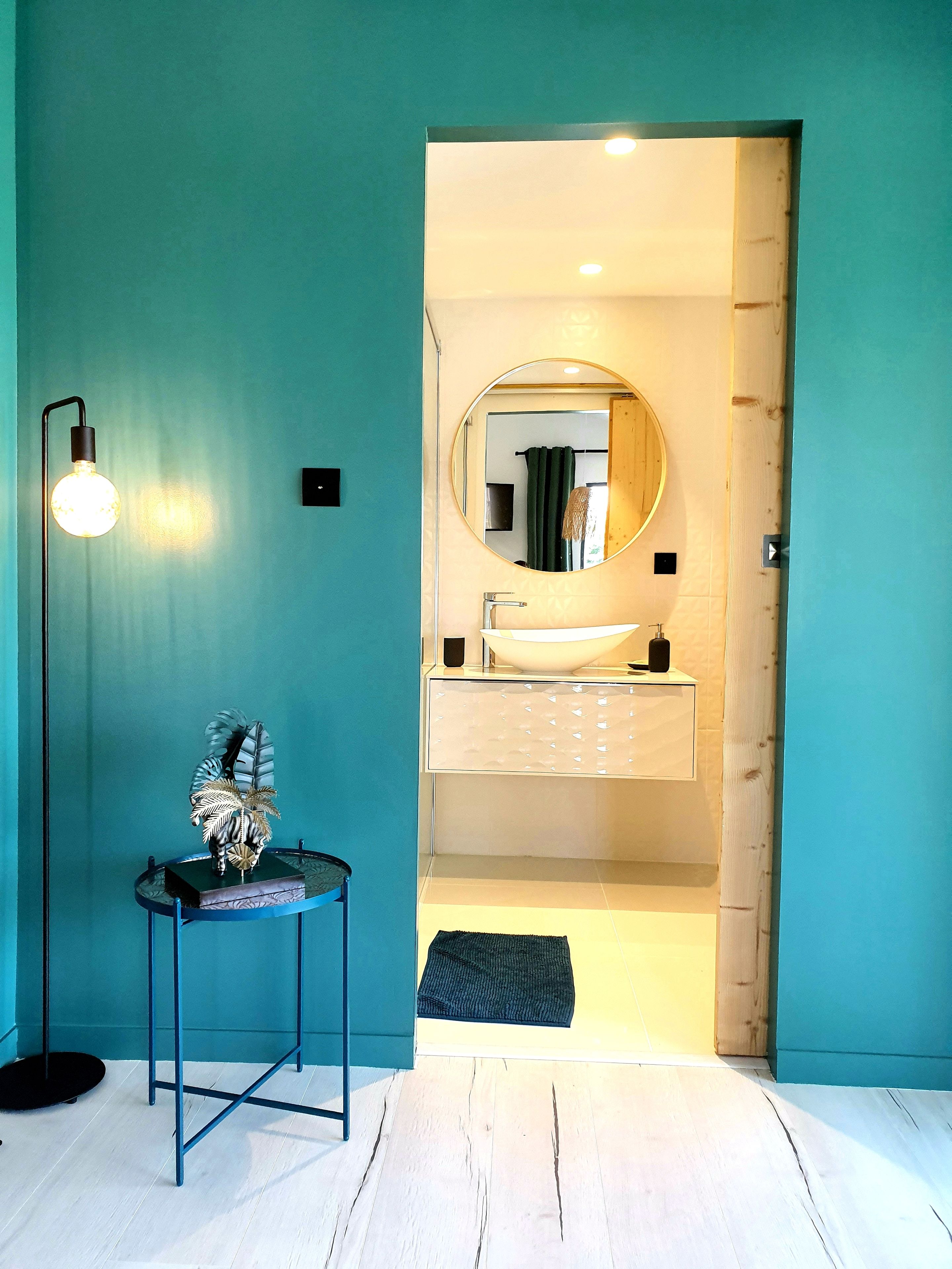 A bathroom with a round mirror, a sink, and a floor lamp.