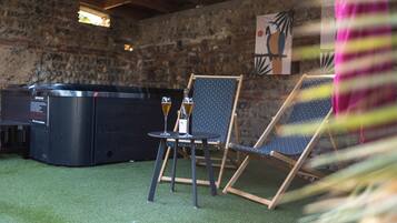 A stone-walled room with a hot tub, two folding chairs, and a small table with glasses.