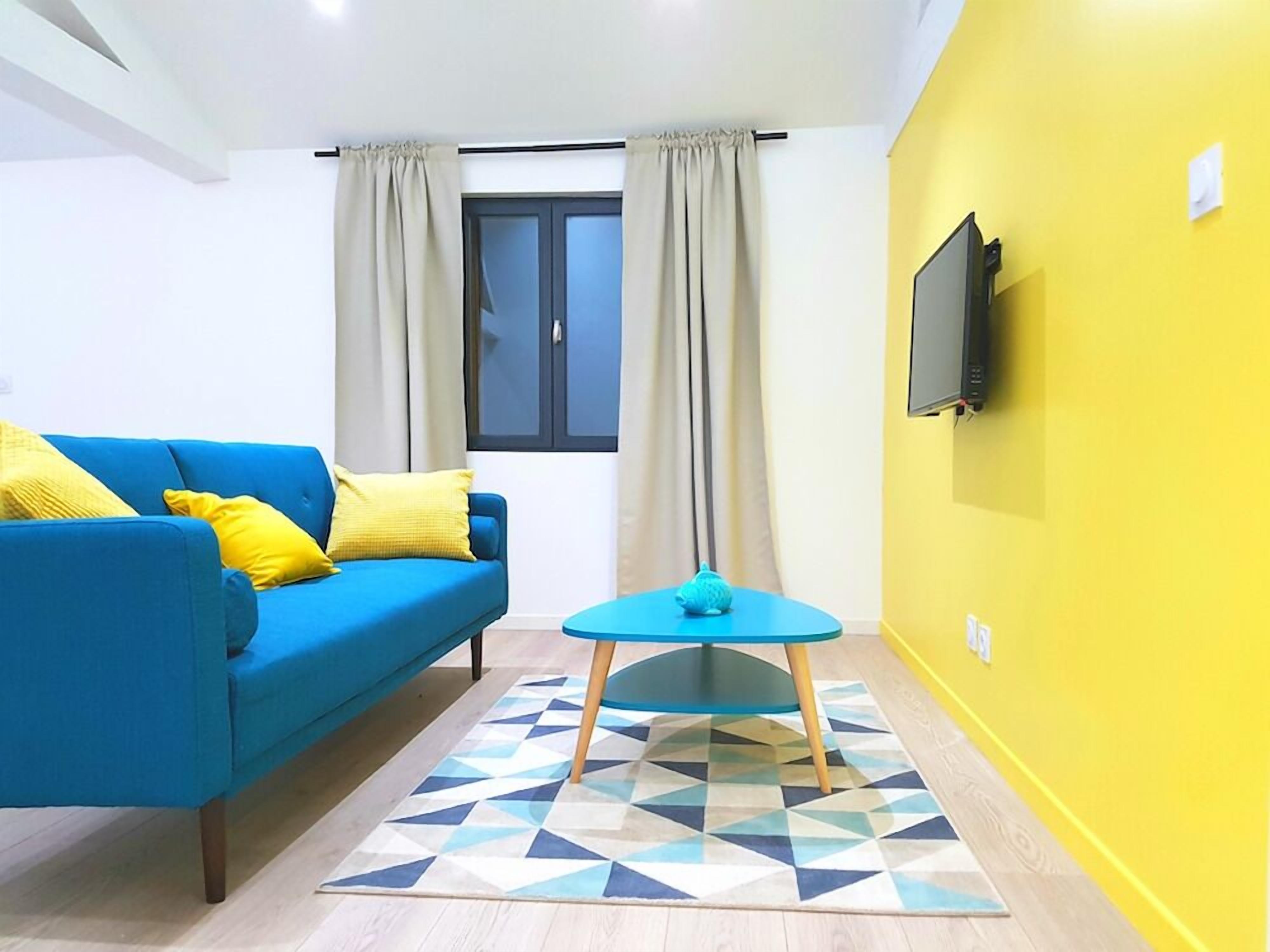 Un salón con un sofá azul, una mesita redonda y un televisor en la pared.