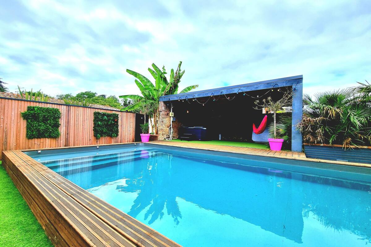A swimming pool with a wooden deck and a covered area with plants.