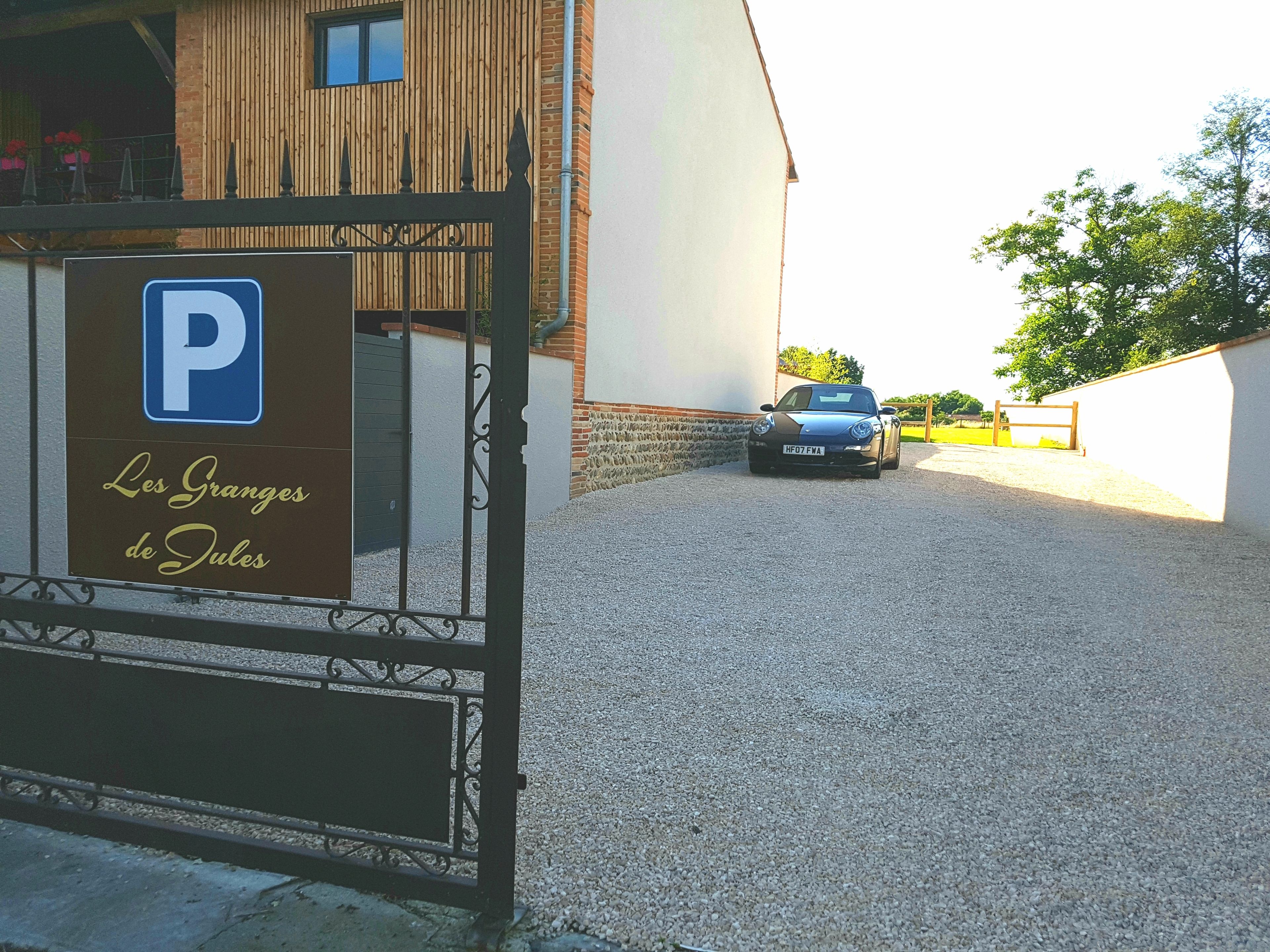 A parking sign for "Les Granges de Jules" with a car parked in front of a building with a white facade and a wooden upper section.