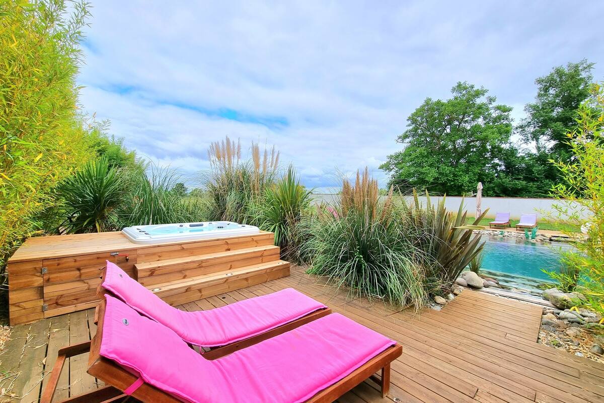 A wooden deck with a hot tub, a lounge chair, and a pool.