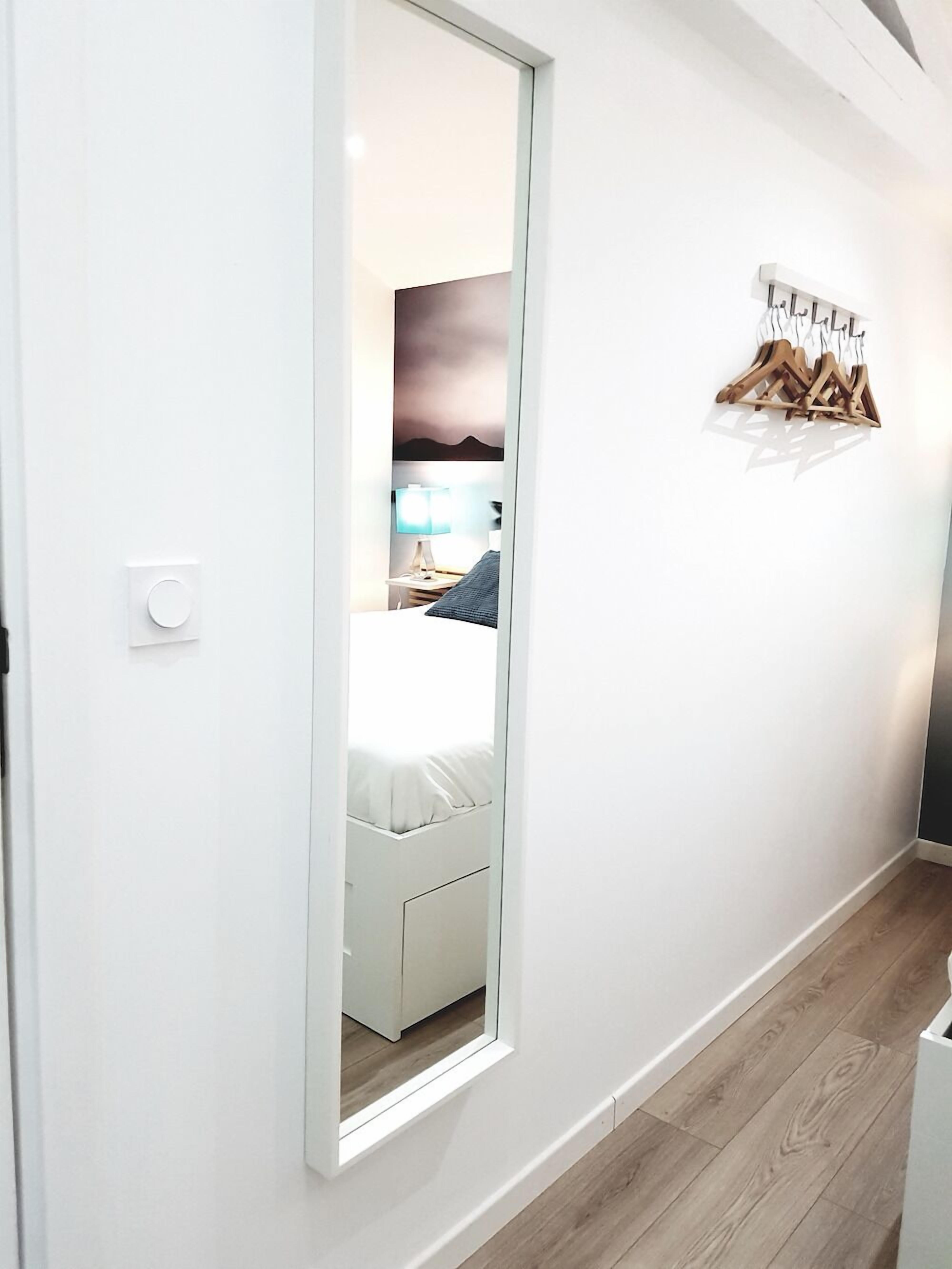 Un pasillo con puerta blanca, suelo de madera y una lámpara fijada a la pared.