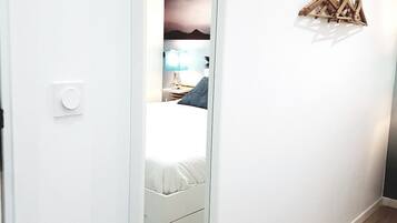 Un pasillo con puerta blanca, suelo de madera y una lámpara fijada a la pared.
