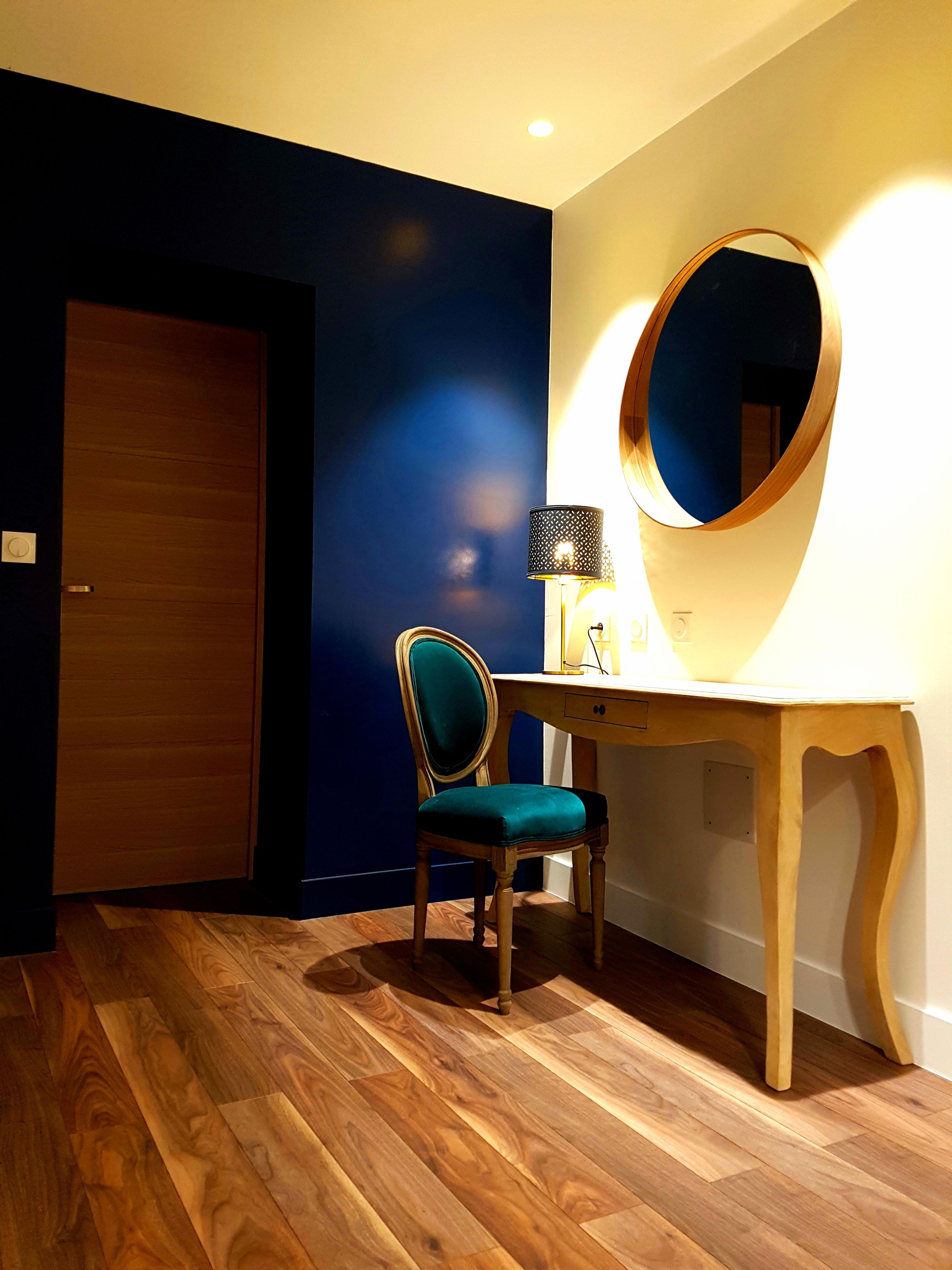 Ein Zimmer mit Holzschreibtisch, Stuhl, Spiegel und Lampe.