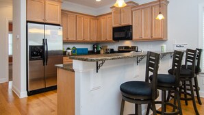 A kitchen with wooden cabinets, stainless steel appliances, a bar area with stools, and pendant lighting. - 4 BR Corner Unit Oceanfront Steps to it all! (Kure Beach)
